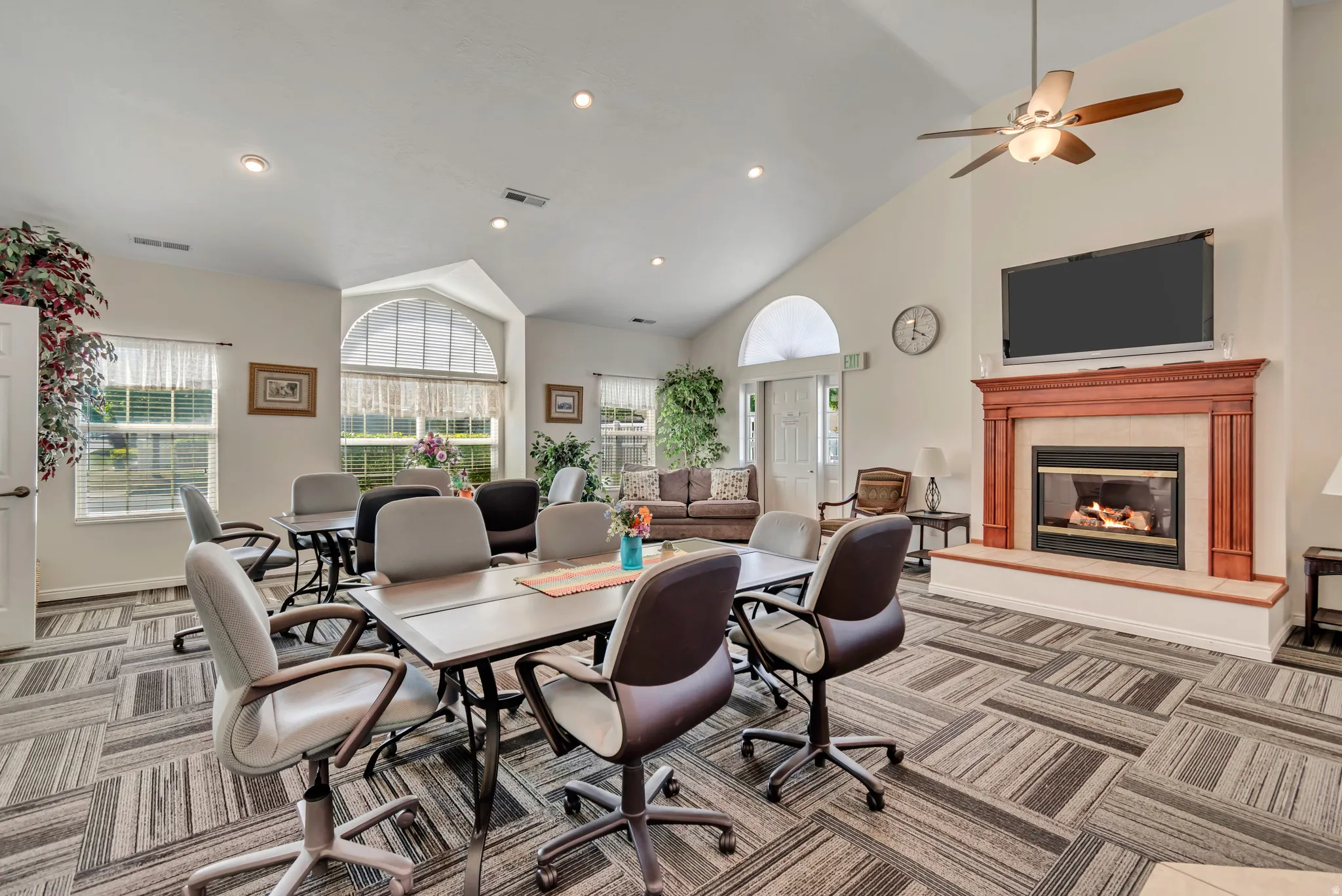 Spacious common area featuring a vaulted ceiling, a gas fireplace with a wood mantle, an arched transom window, recessed lighting, and patterned carpet flooring