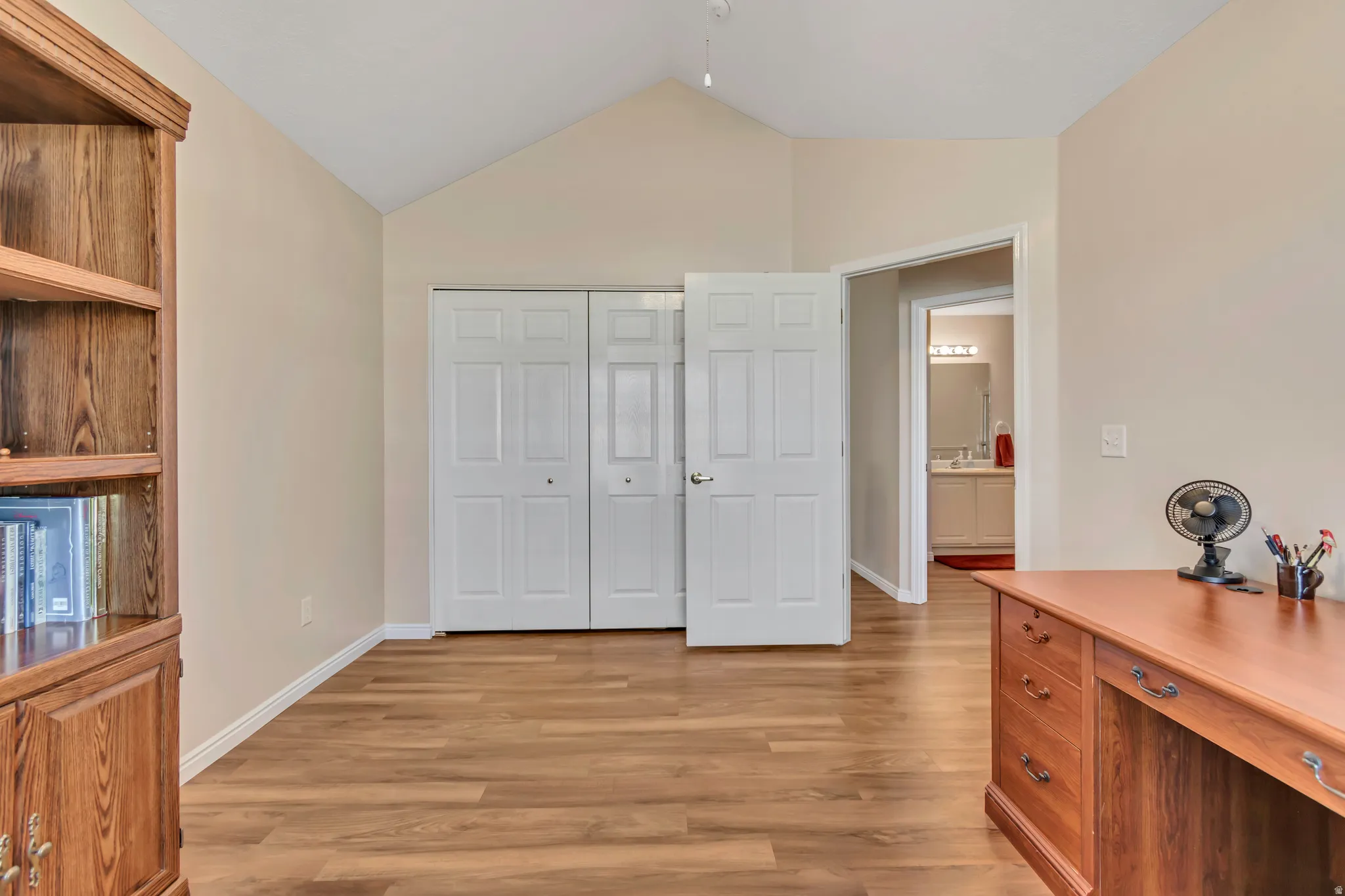 Vaulted ceiling room featuring wood-finish flooring, neutral wall tones, and a double closet with bi-fold doors