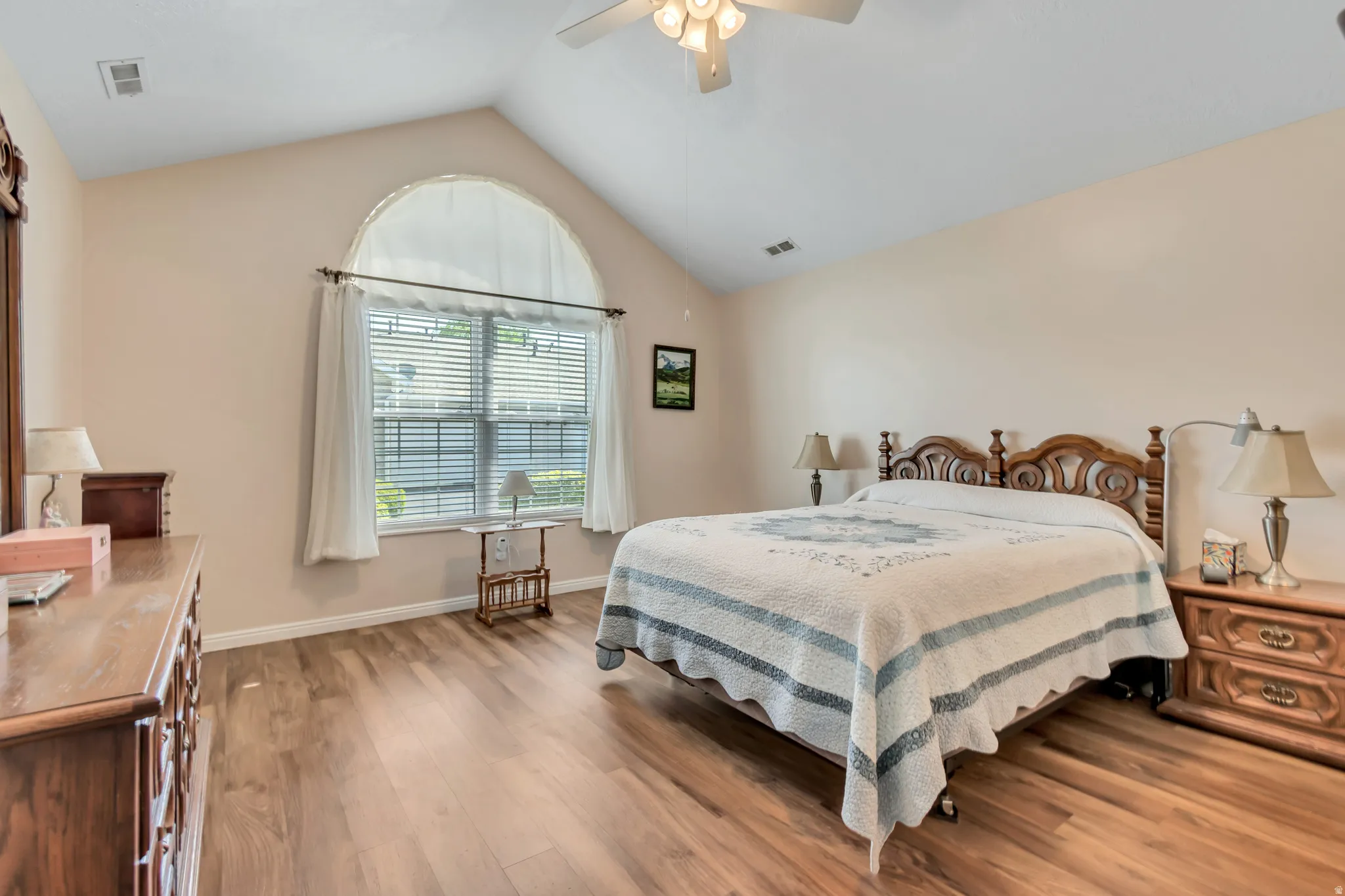 Vaulted ceiling room featuring wood-finish flooring, an arched top window, and a ceiling fan with integrated lighting
