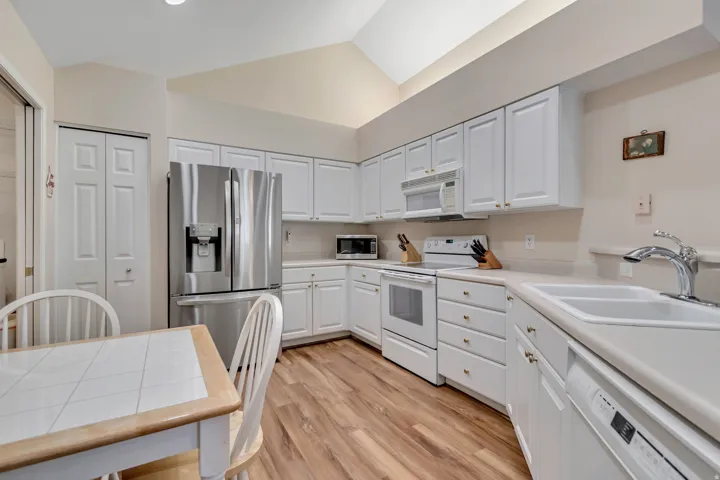 Kitchen featuring white cabinetry with gold-toned hardware, wood-finish flooring, a stainless steel French door refrigerator, white range, and a double-basin sink