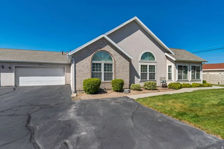 Exterior featuring stucco and brick accents, an arched window, a two-car garage, and a concrete walkway