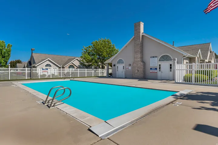 Rectangular swimming pool with a diving board and built-in entry steps, surrounded by a concrete deck and white picket fencing