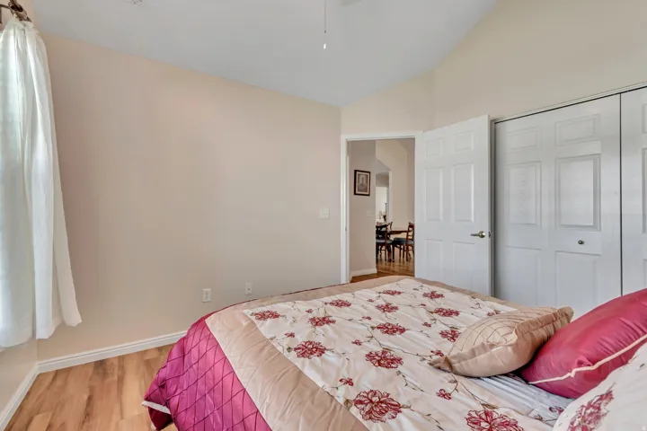 Bedroom featuring vaulted ceilings, wood-finish flooring, and white bi-fold closet doors