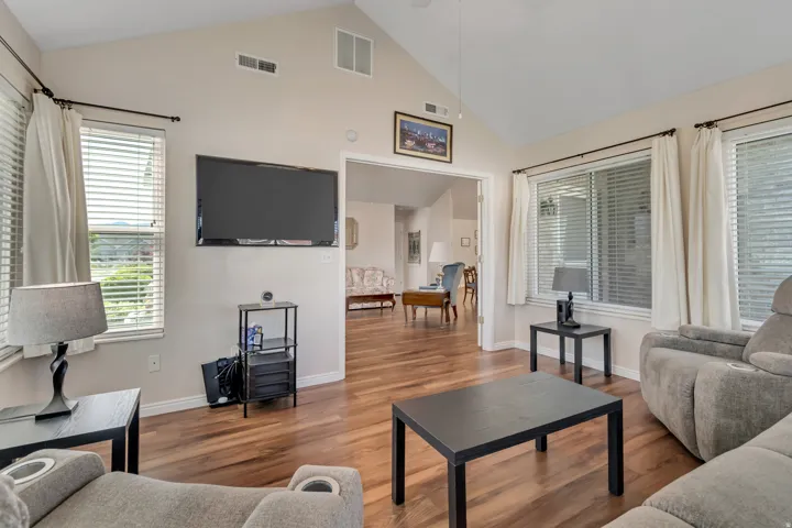 Living area featuring vaulted ceilings, wood-finish flooring, numerous windows with blinds, and white trim