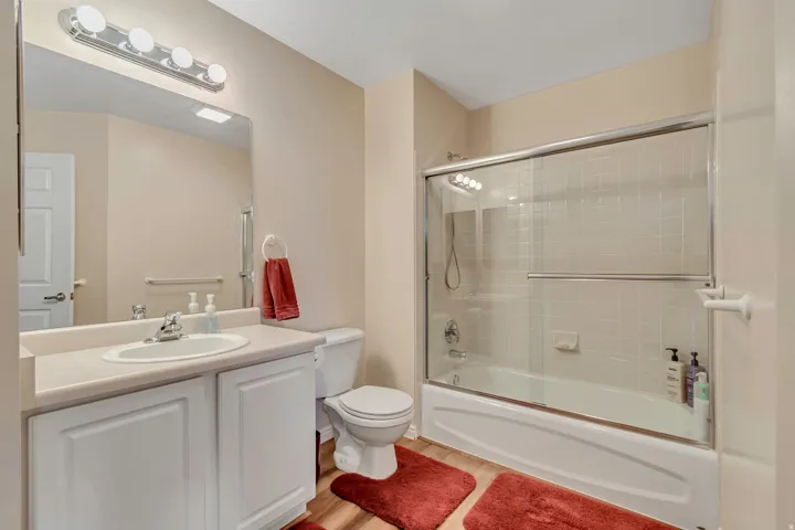 Full bathroom featuring a single vanity with a white countertop and base cabinetry, a wall-mounted mirror with overhead light bar, a toilet, and a combined bathtub and shower with sliding glass doors