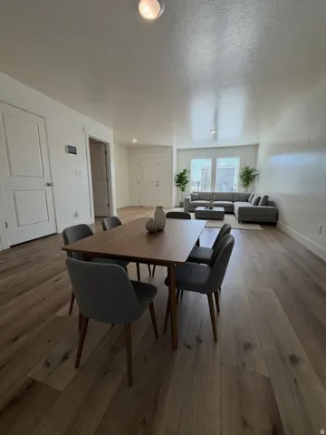 Open-concept living area featuring wood-finish flooring throughout, a dining table with seating for four, and a sectional sofa arrangement  Thank you to AI for the photographic possibility.