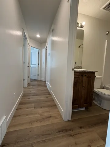 Hallway featuring wood-finish flooring, recessed lighting, and white baseboards
