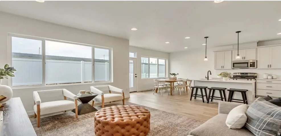 Open-concept living space with light wood-finish flooring, recessed lighting, and expansive windows.Picture is of a similar home.