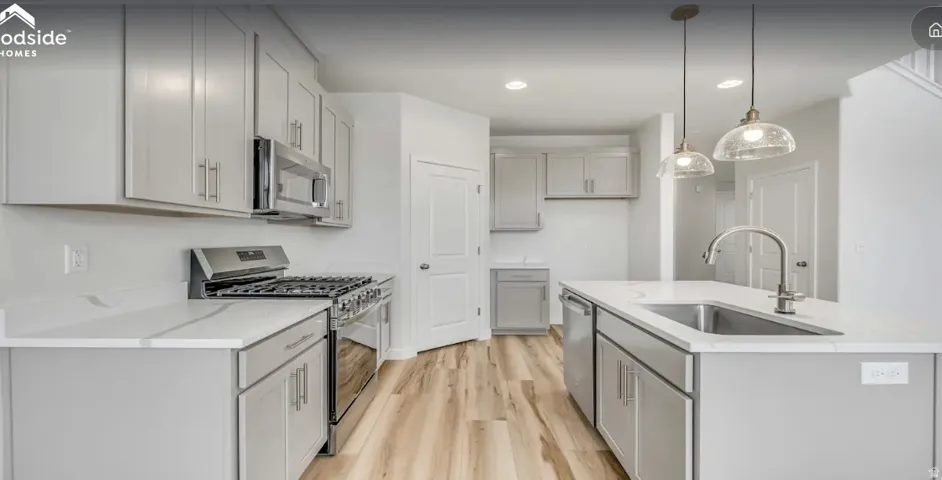 Modern kitchen featuring light gray cabinetry, stainless steel appliances, and a central island with an undermount sink.  Picture is of a similar home.