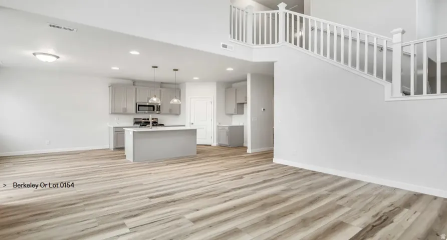 Open-concept living space featuring wood-finish flooring, a kitchen island with pendant lighting, light gray cabinetry, and stainless steel appliances.  Picture is of a similar home.