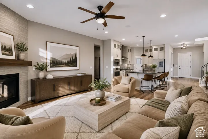 Open-concept living space featuring wood-finish flooring, a contemporary fireplace with a textured surround, and a ceiling fan
