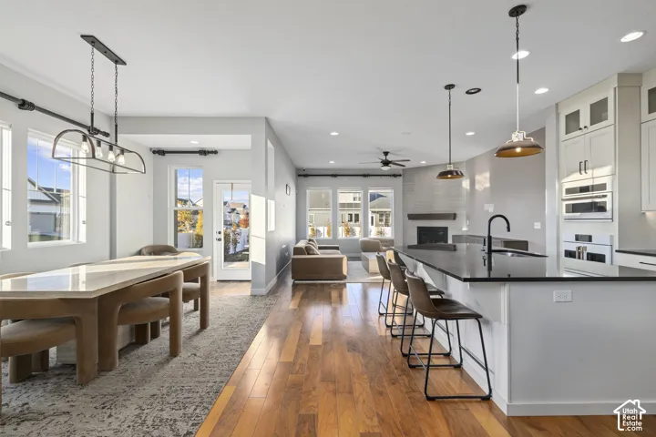 Open-concept living space featuring wood-finish flooring, a kitchen island with seating, pendant lighting, and a fireplace with a mantel
