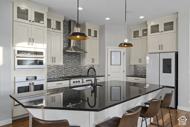 Kitchen featuring a large central island with a dark countertop, white cabinetry with glass-front uppers, stainless steel appliances, and a mosaic tile backsplash