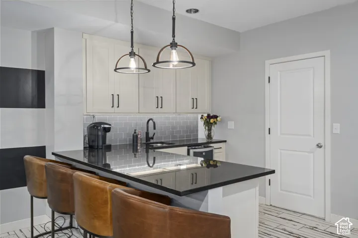 Kitchenette featuring a black countertop, grey subway tile backsplash, white shaker-style cabinetry with matte black hardware, and two pendant light fixtures