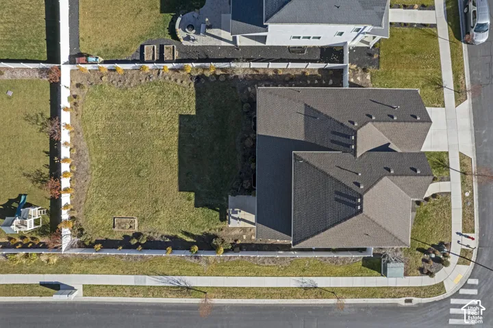 Dark shingle roof, concrete sidewalks, white fencing, and a manicured lawn