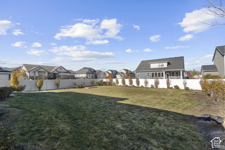 Expansive manicured lawn with mature landscaping and seasonal plantings, backing a two-story residence featuring a dark-shingled roof, white exterior trim, and dormer windows