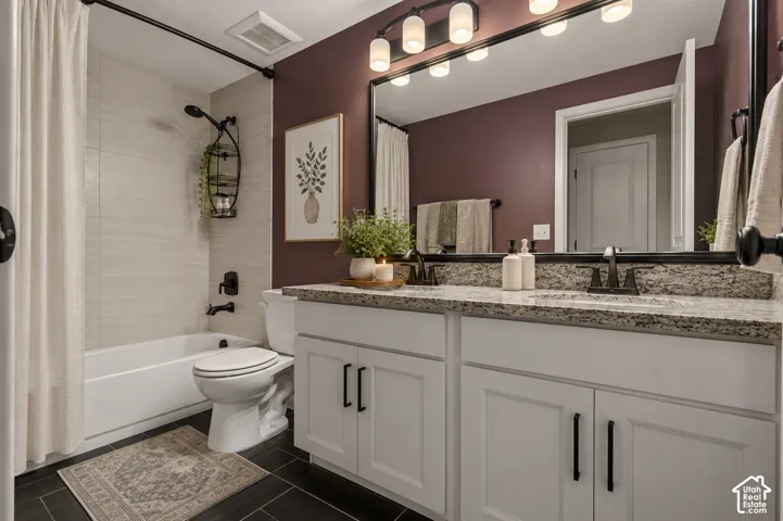 Double vanity with a speckled countertop, white cabinetry with dark hardware, and a large mirror