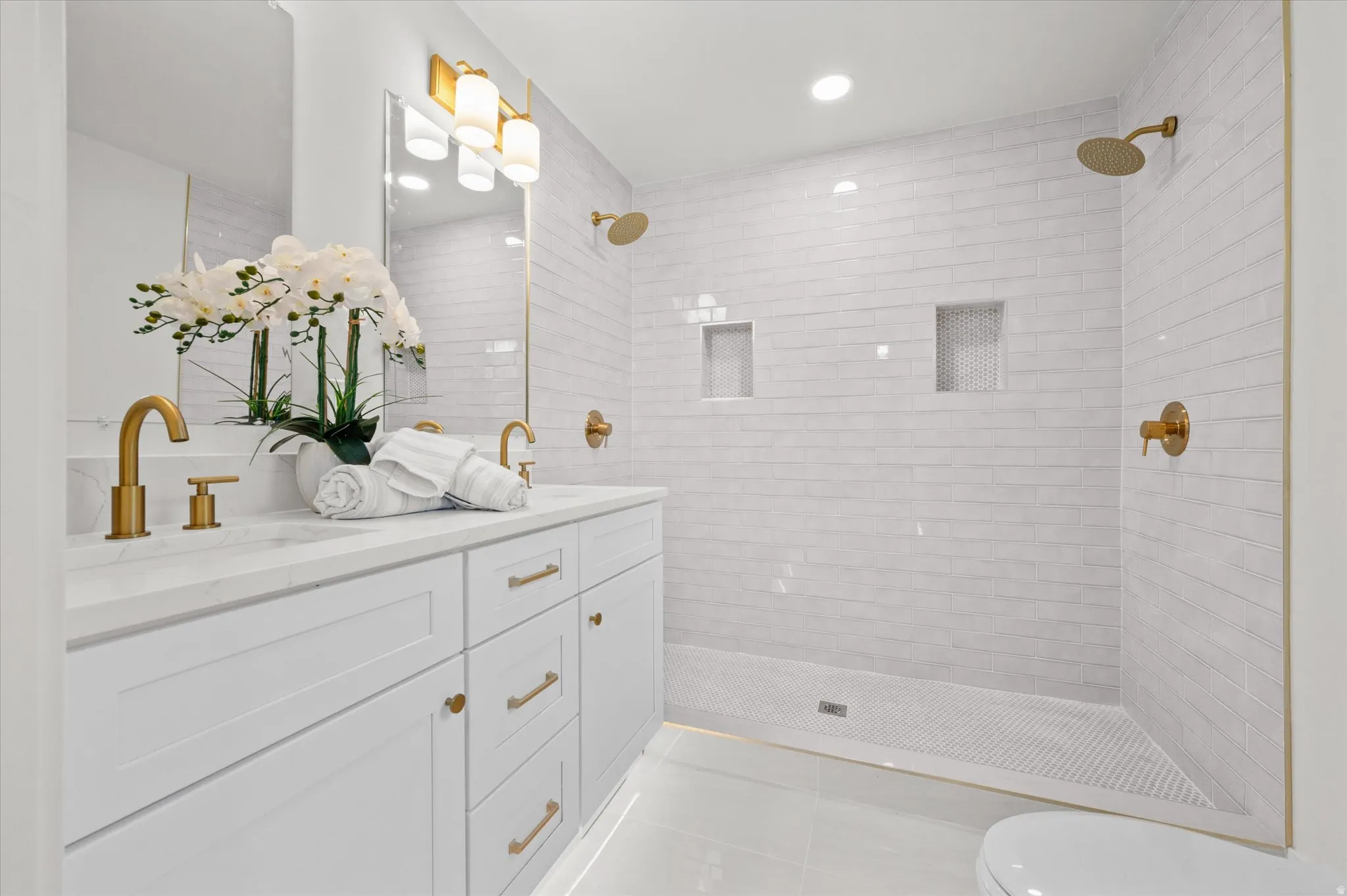 Bright bathroom featuring a double vanity with white cabinetry, gold-finish hardware, and a quartz countertop