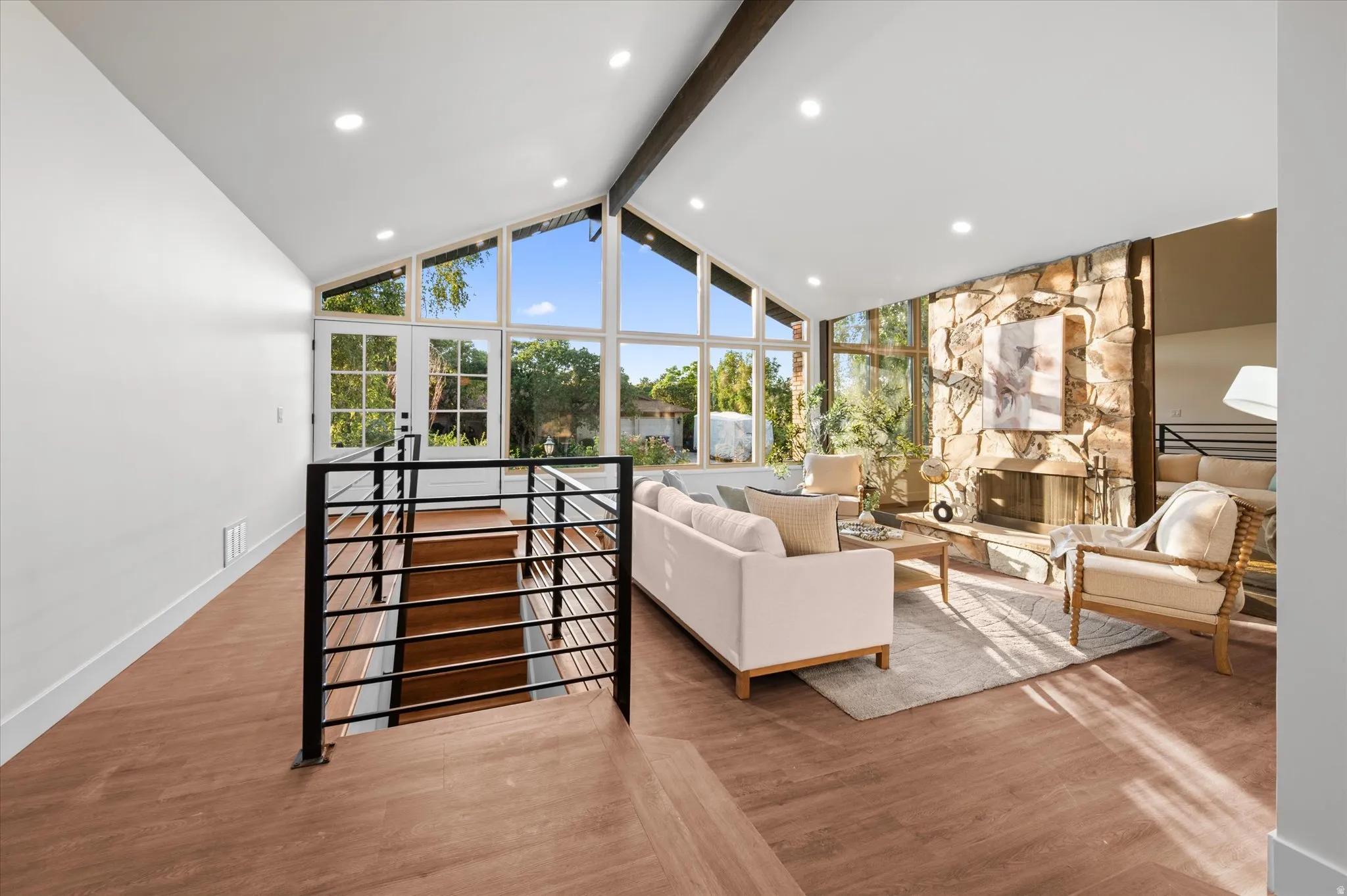Vaulted ceilings with exposed wood beams, a stone-accented fireplace, and expansive windows characterize this living space