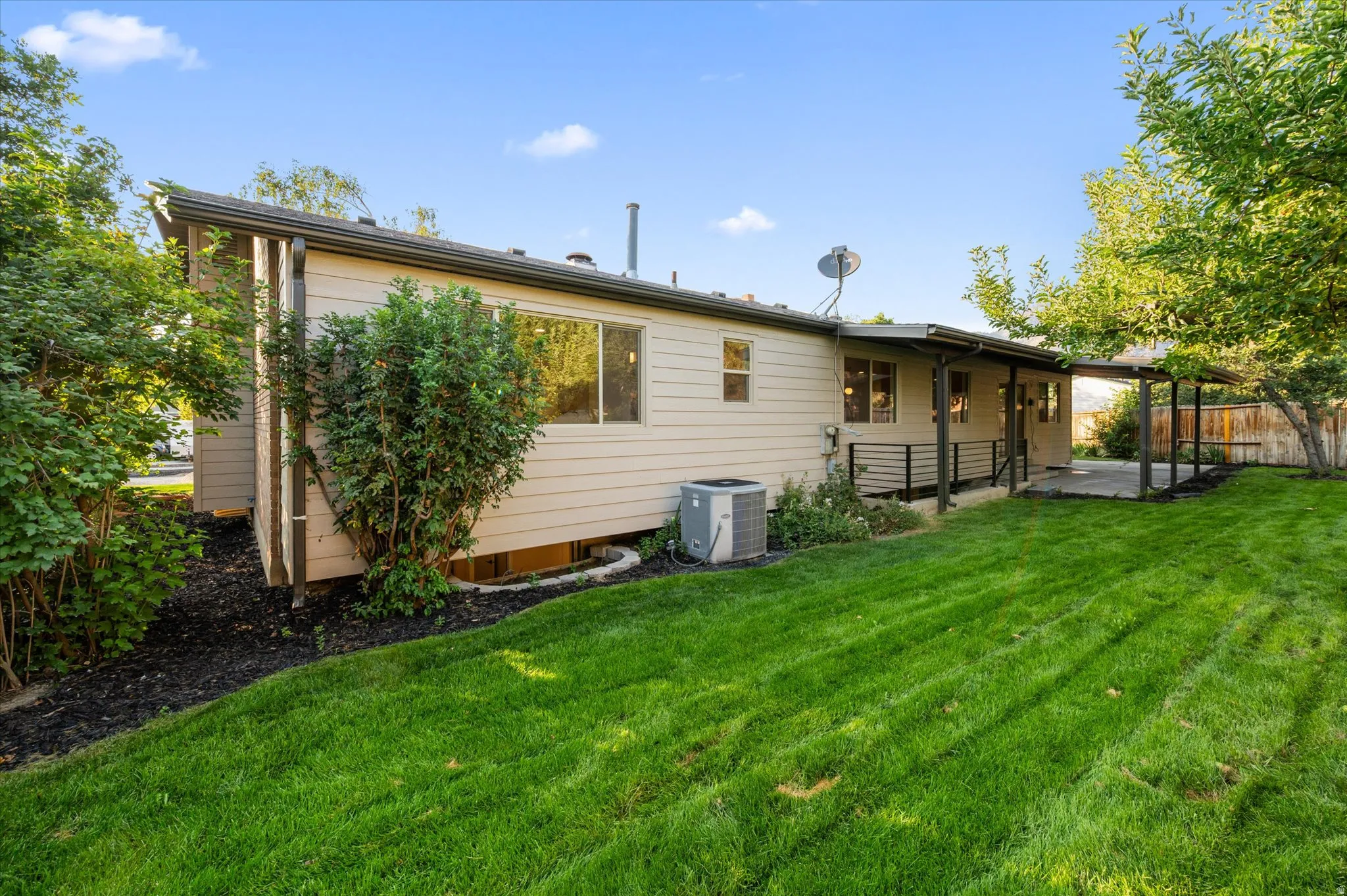 Expansive green lawn with a covered patio, mature trees, and a well-maintained exterior facade