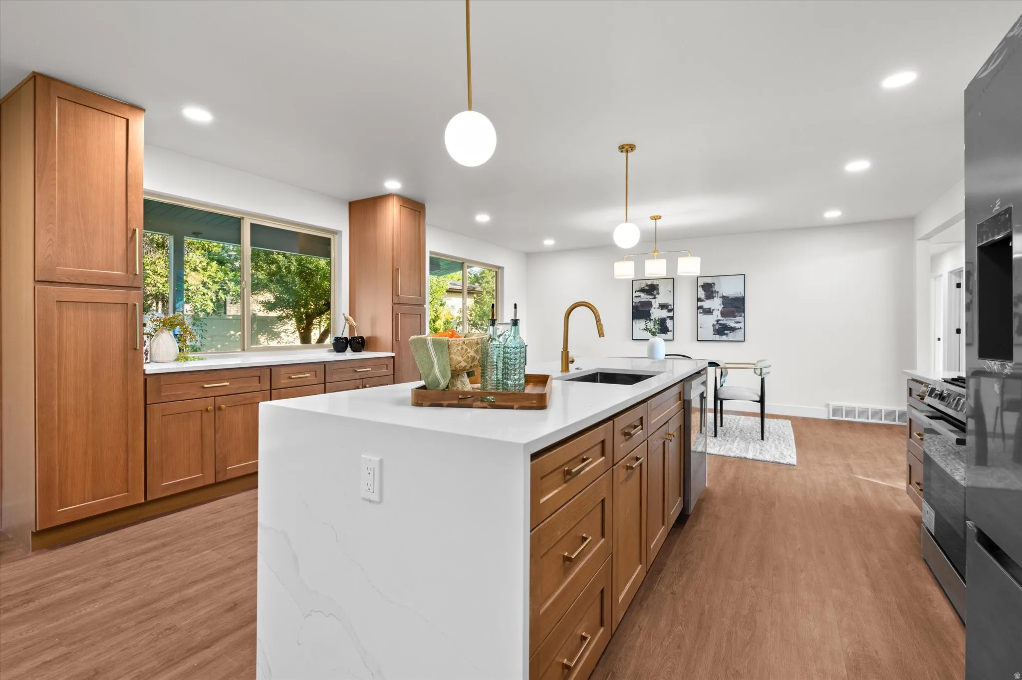 Modern kitchen featuring a large center island with a white countertop and integrated sink, gold-finish fixtures, wood-finish flooring, and recessed ceiling lighting
