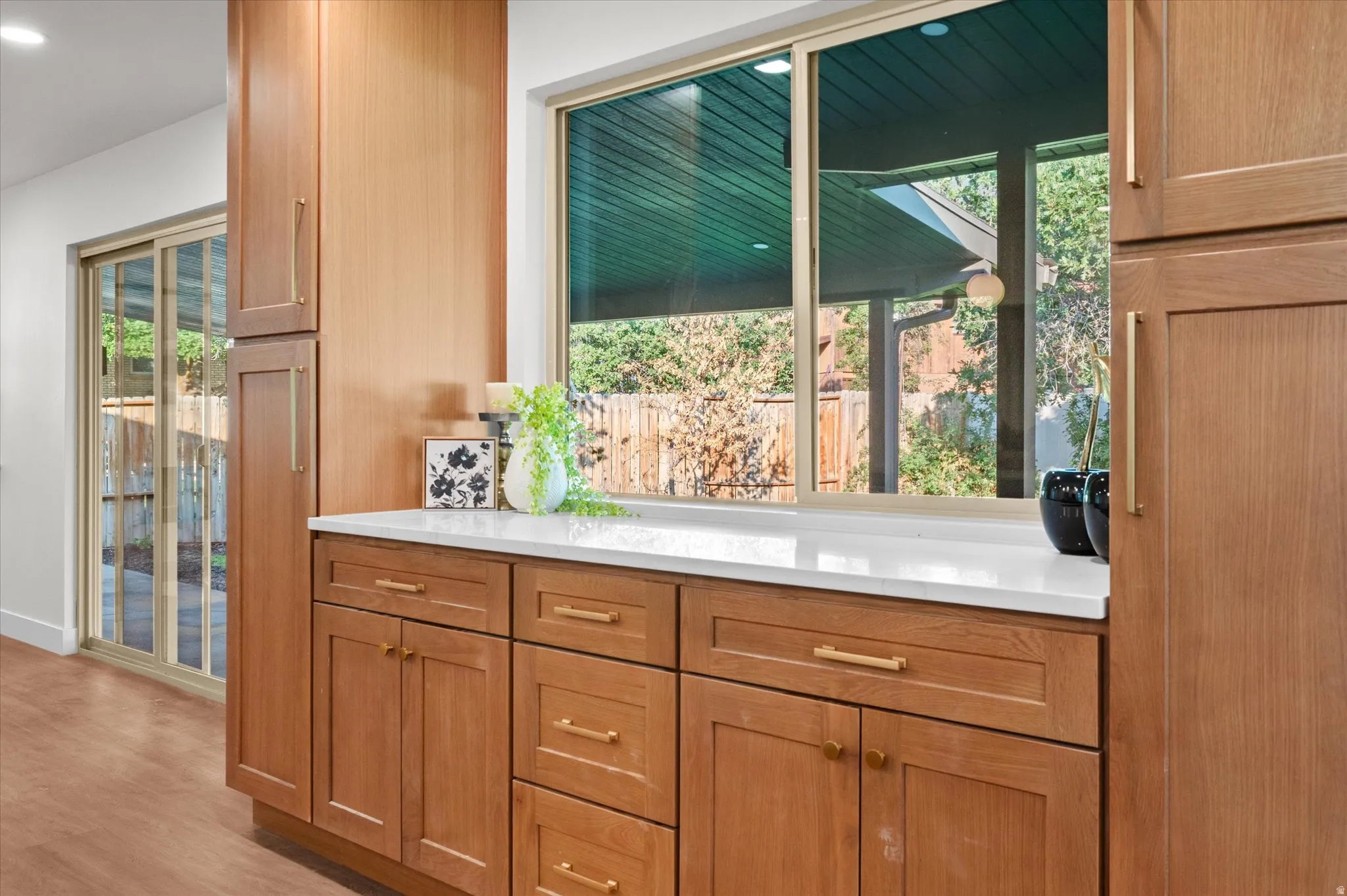 Kitchen featuring wood-finish cabinetry with gold-tone hardware, white countertops, and a large window overlooking the exterior
