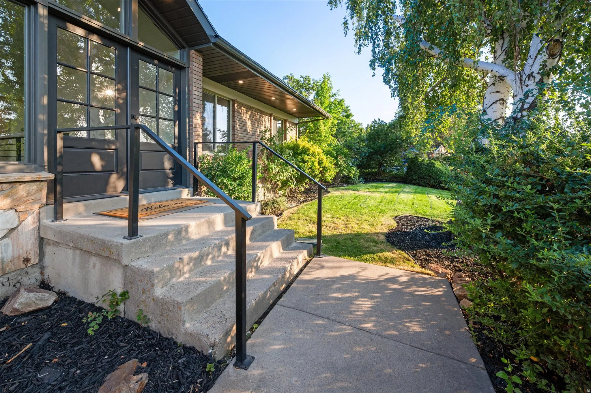 Entryway featuring concrete steps with black metal railings, a full-light front door with transom windows, and a manicured lawn area