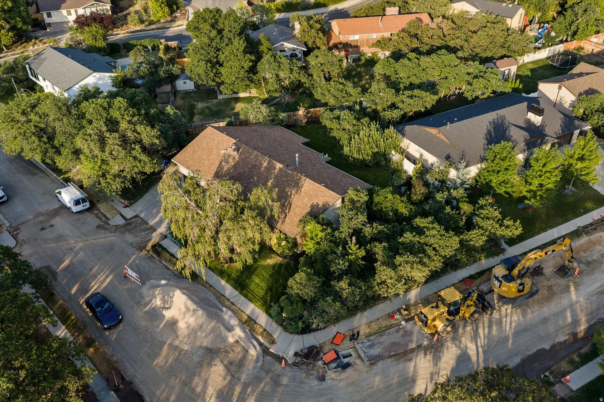 Gable roof residence featuring a mature tree-lined lot, green lawn, and concrete sidewalks