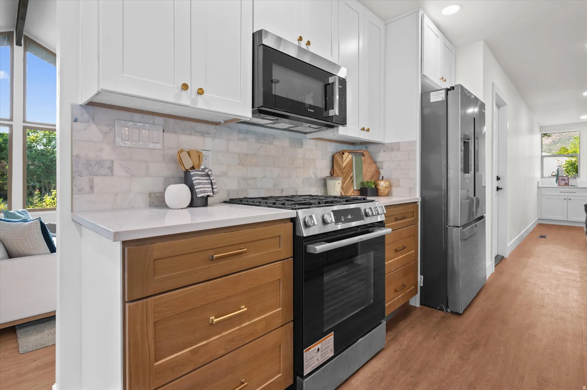 Kitchen featuring white upper cabinetry, wood-finish lower cabinetry, a stone tile backsplash, and stainless steel appliances
