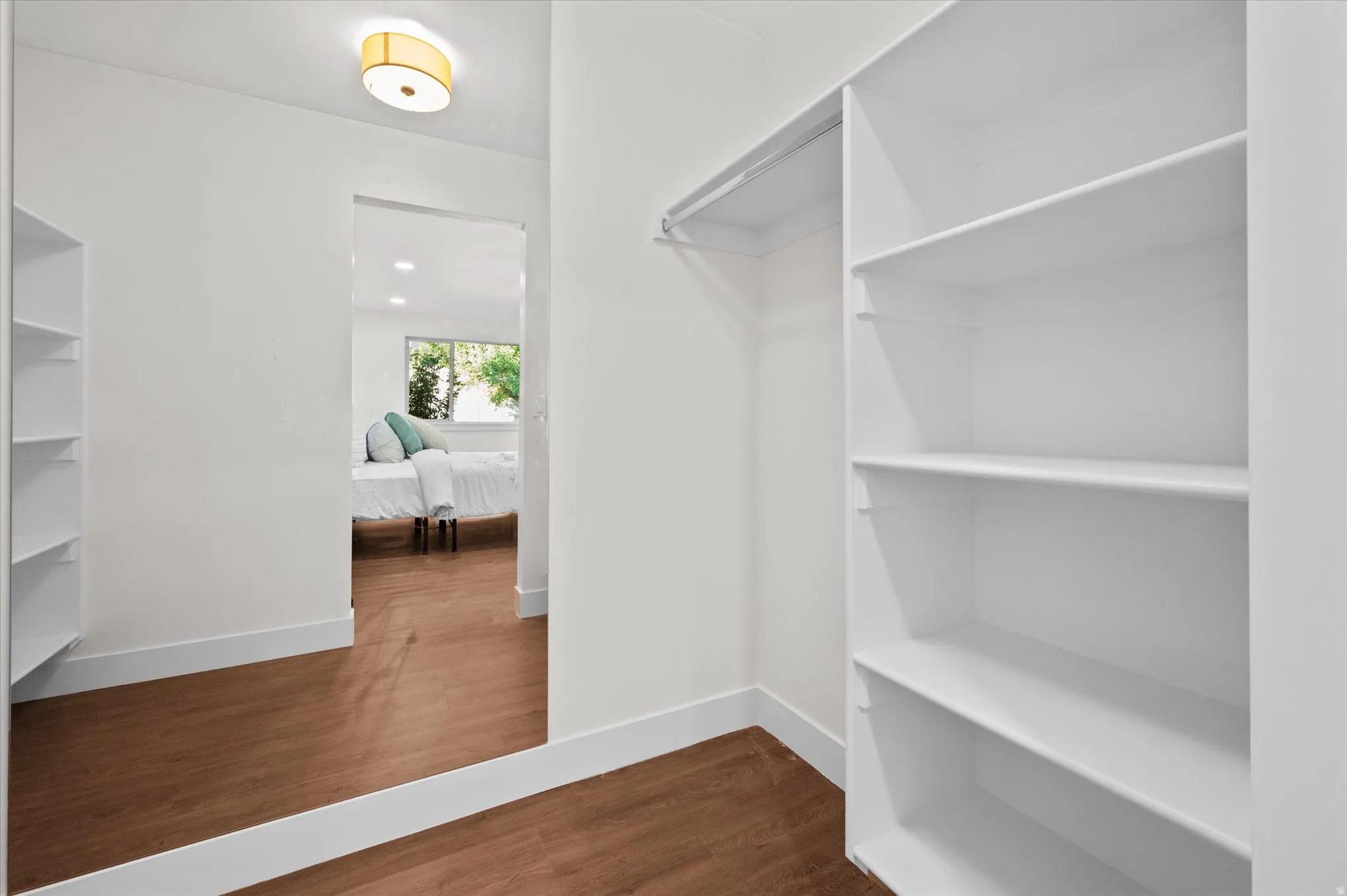 Walk-in closet featuring built-in shelving, hanging rod, and wood-finish flooring