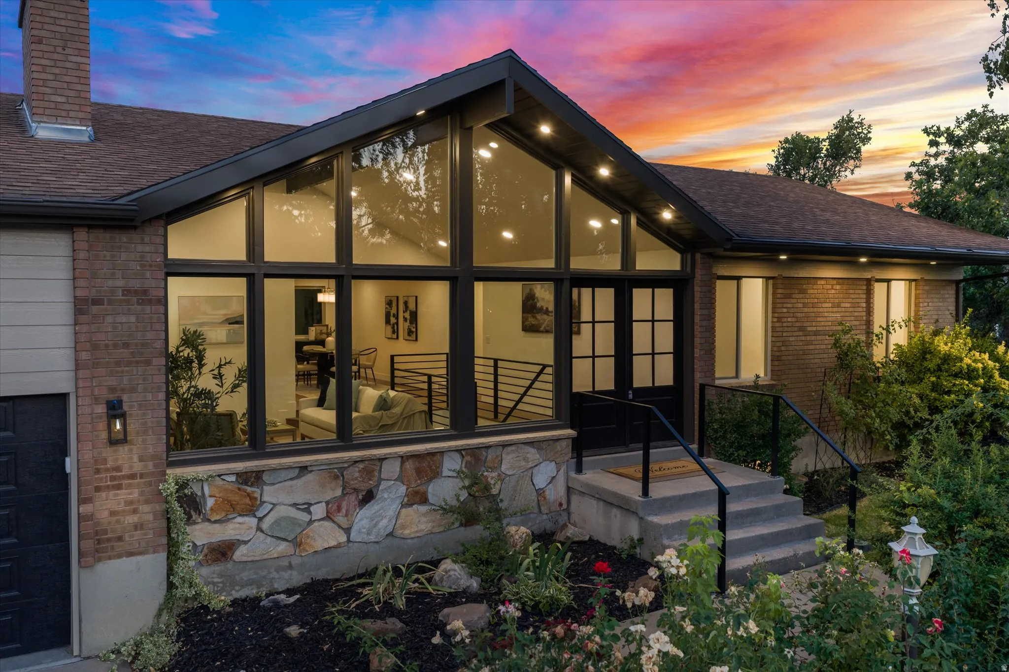 Contemporary exterior featuring a striking A-frame window wall, brick and stone facade, dark-frame windows, and a black double-door entry