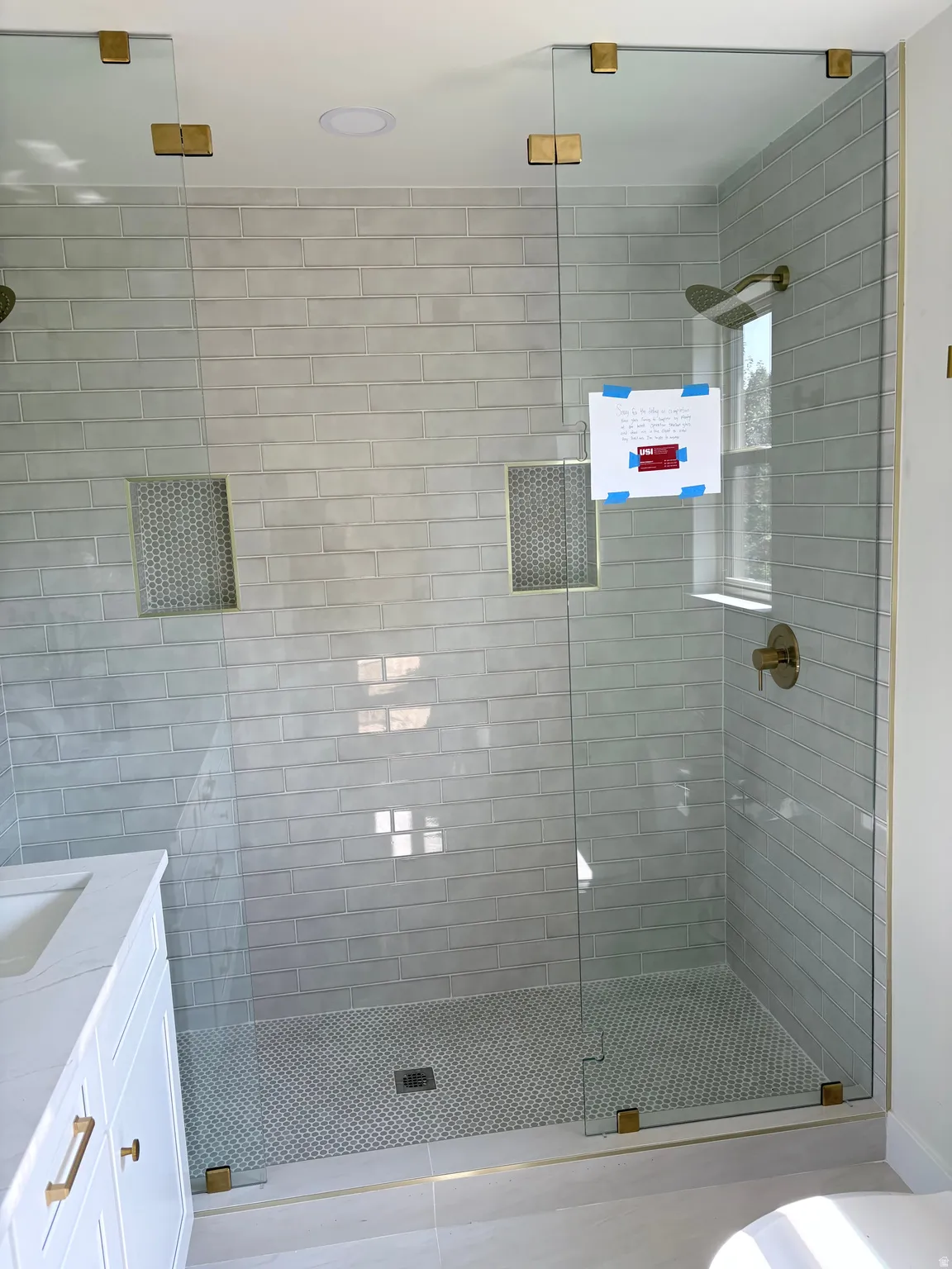 Glass-enclosed shower with subway tile walls, dual shower niches, and a penny tile floor