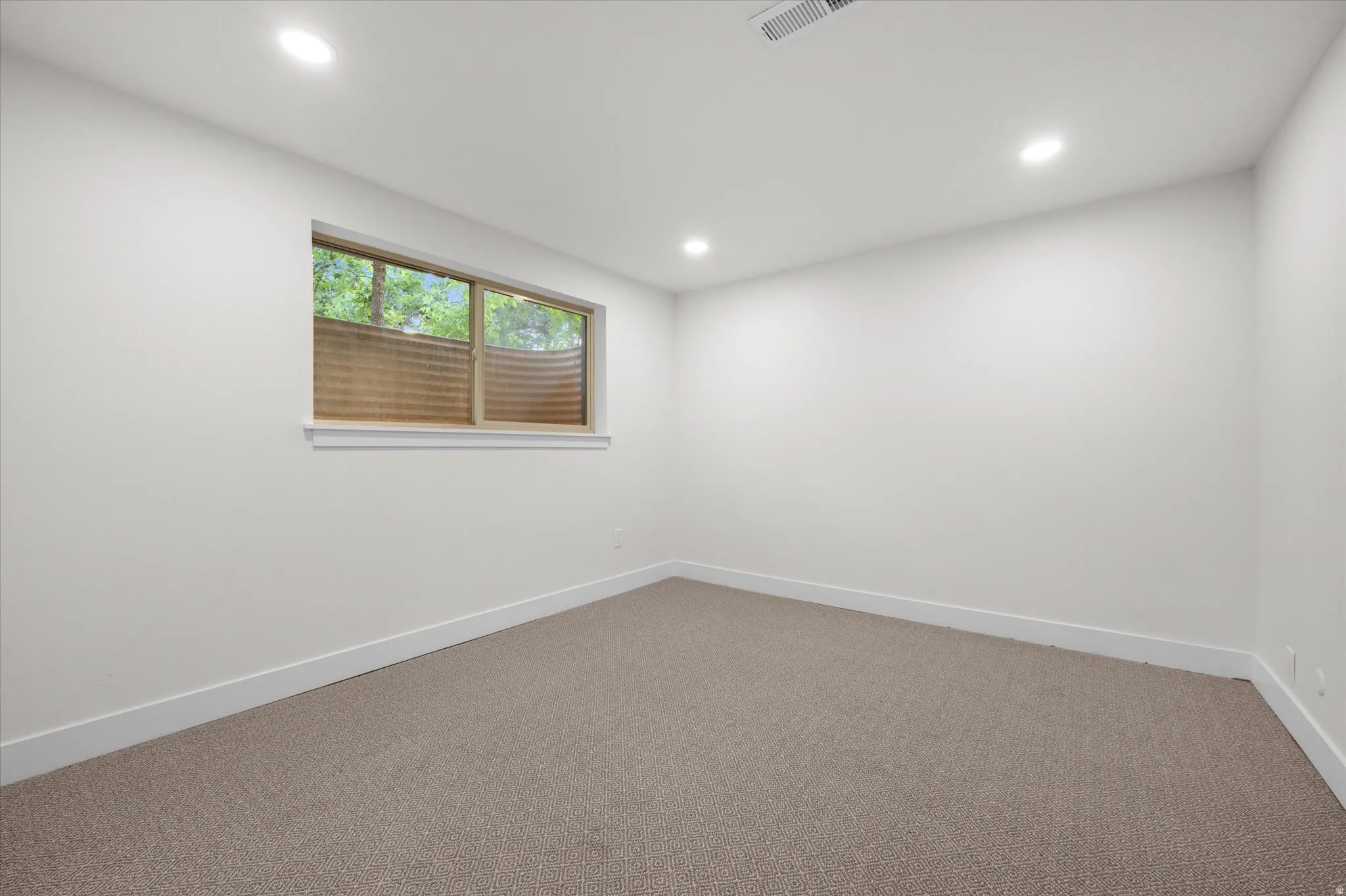 Carpeted room with a horizontal window featuring a window well