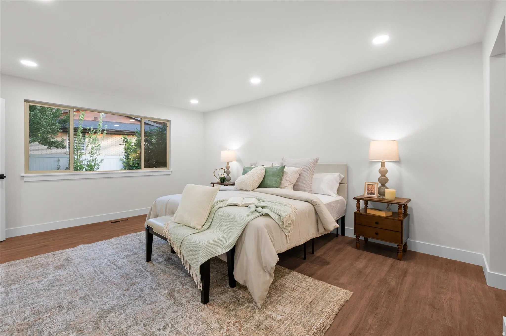 Spacious room featuring wood-finish flooring, a large window, recessed lighting, and white baseboards
