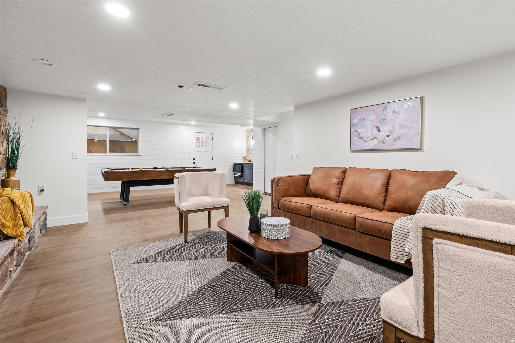 Spacious recreational room featuring wood-finish flooring, recessed lighting, a stone-front fireplace, and white shiplap accent wall