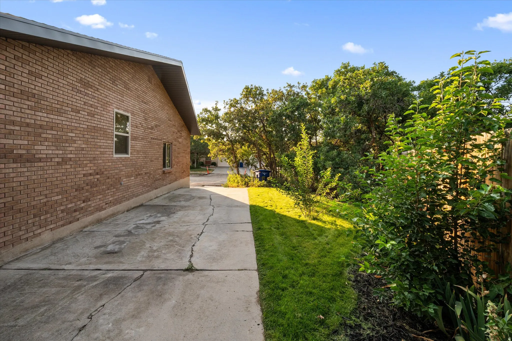Brick exterior with a gabled roofline, concrete driveway, and a landscaped side yard featuring mature trees and established plantings