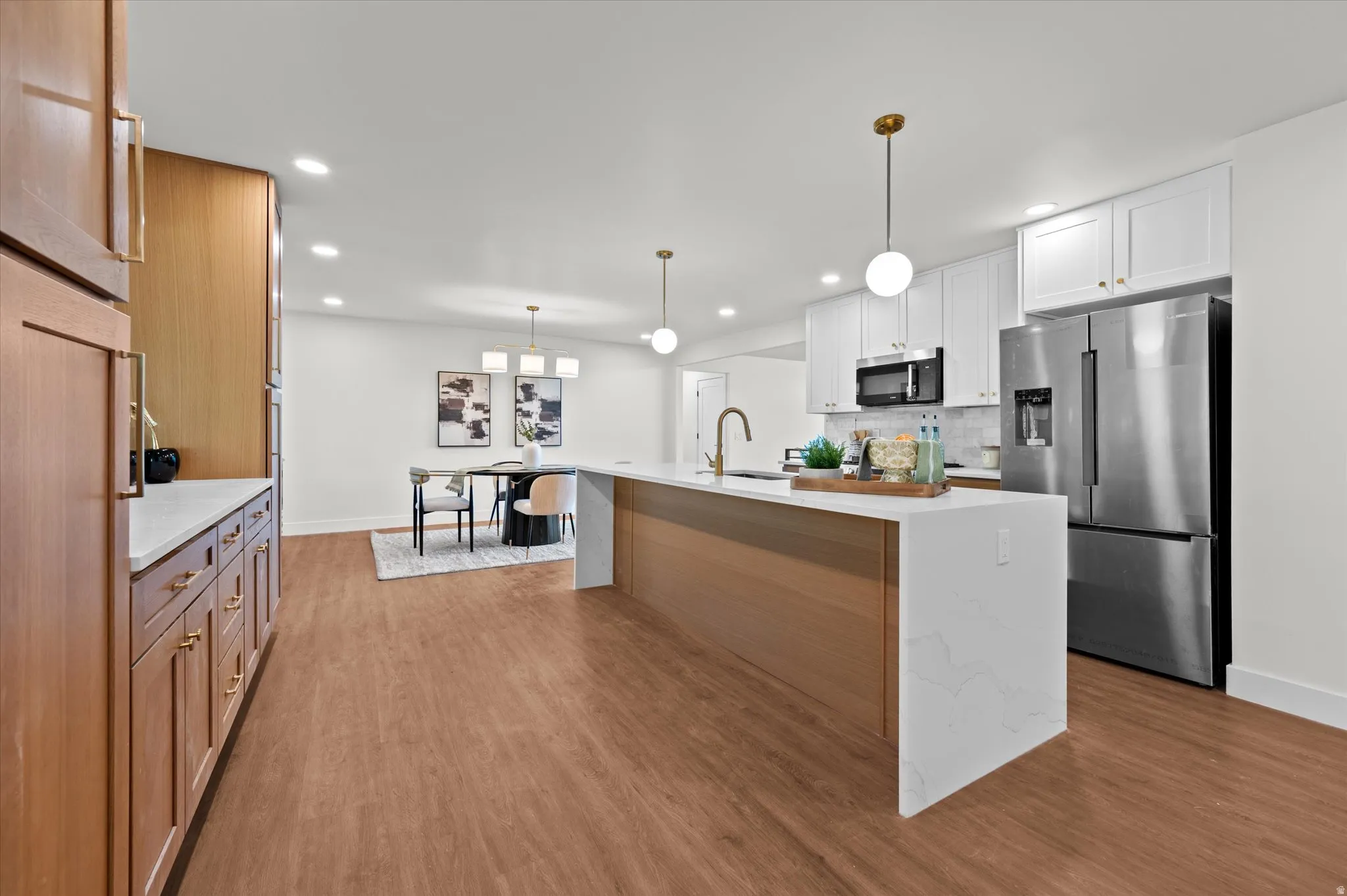Open concept kitchen featuring an expansive island with a waterfall countertop, wood-finish flooring, recessed lighting, white upper cabinetry, and stainless steel appliances
