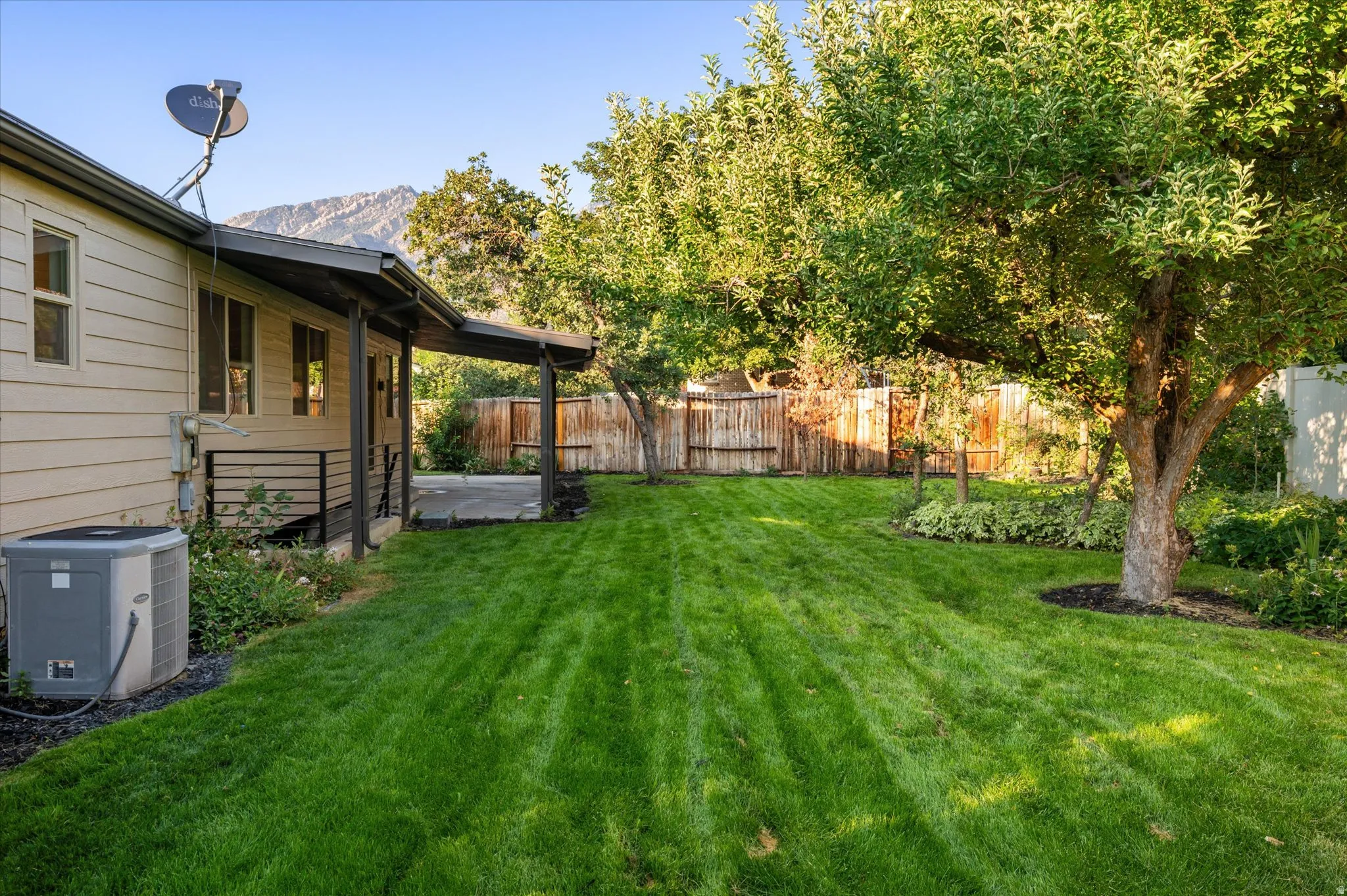 Expansive green lawn with mature trees and a covered patio, framed by a wooden privacy fence
