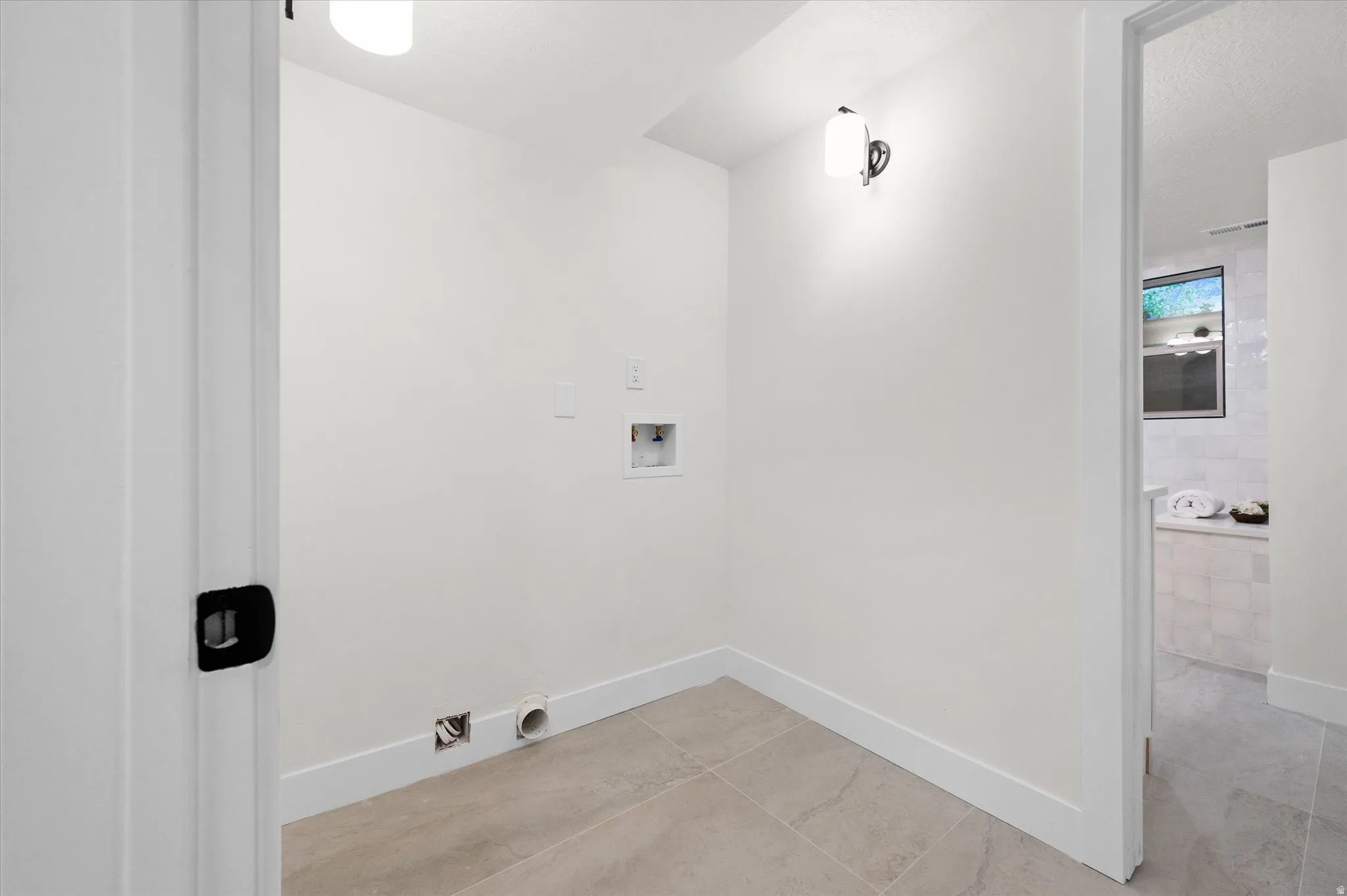 Dedicated utility space featuring tile flooring, white walls, and a modern wall sconce