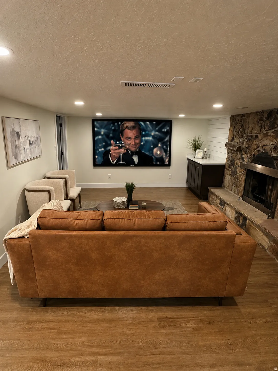 Entertainment space featuring a large wall-mounted screen, wood-finish flooring, recessed lighting, and a stone-clad fireplace