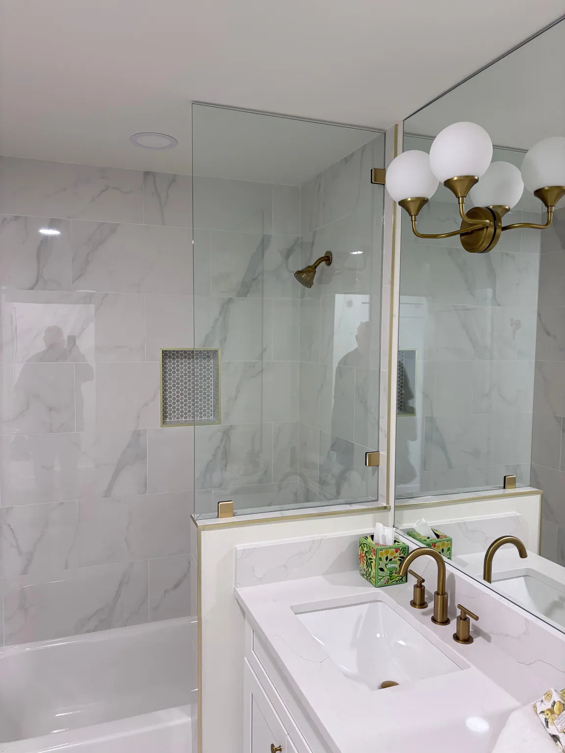 Sleek bathroom featuring a built-in tub with a glass shower panel, white marble-style wall tiling, and a vanity with an integrated sink