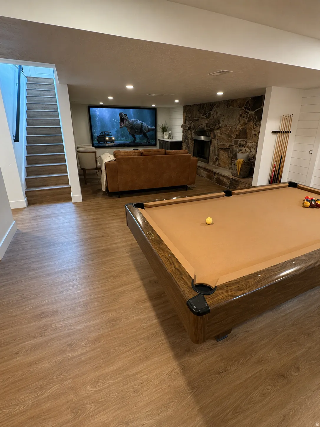 Entertainment area featuring wood-finish flooring, a stone-clad fireplace, a large projection screen, recessed lighting, and white shiplap accent walls