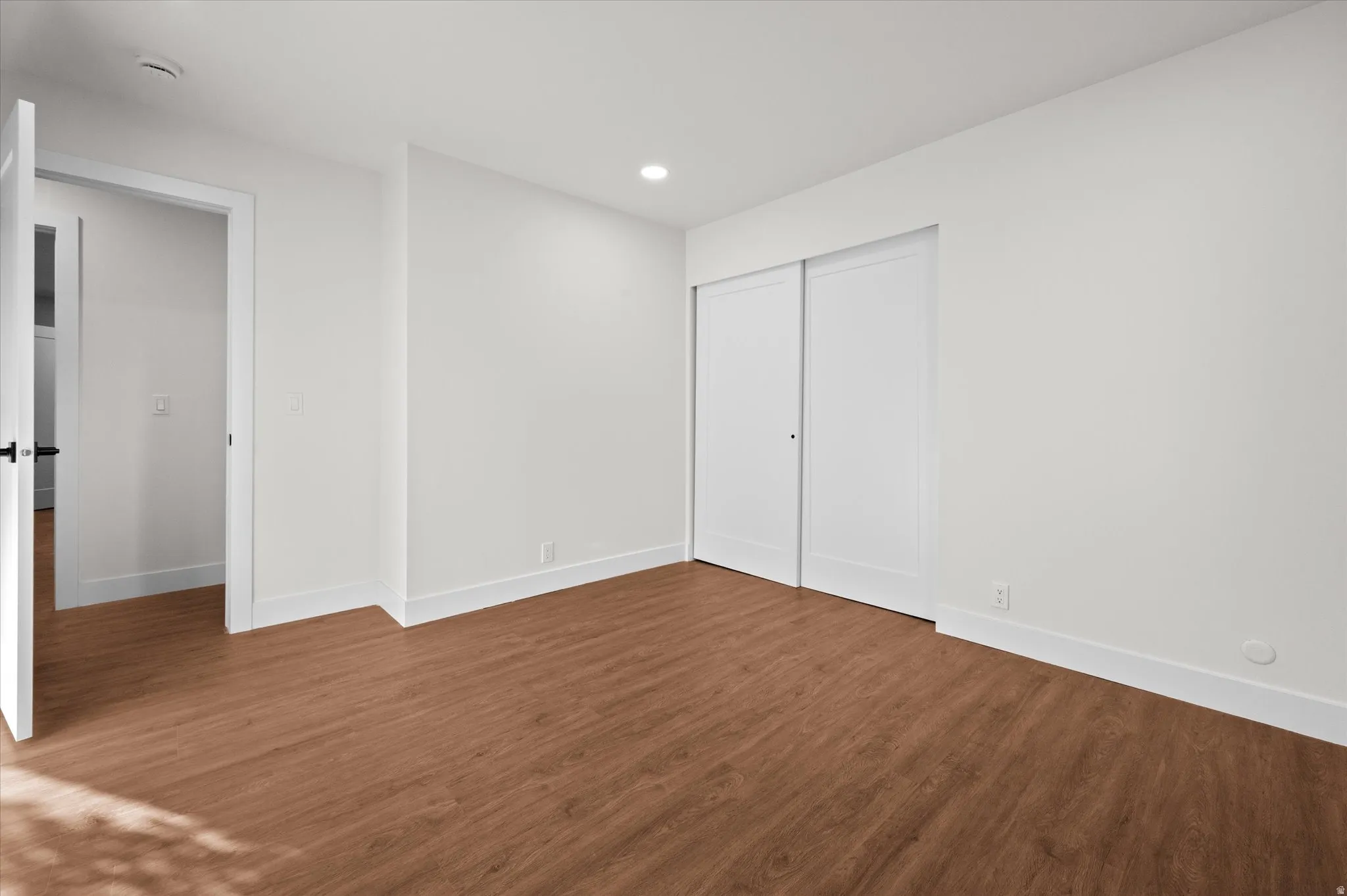 Spacious room featuring wood-finish flooring, crisp white walls, recessed lighting, and a double sliding closet door