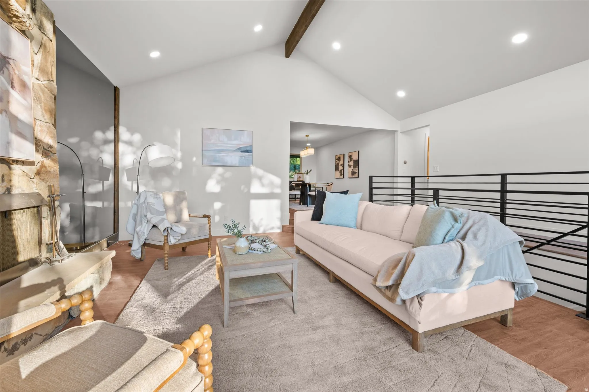 Living area featuring a stone fireplace, vaulted ceiling with exposed wood beams, wood-finish flooring, and recessed lighting