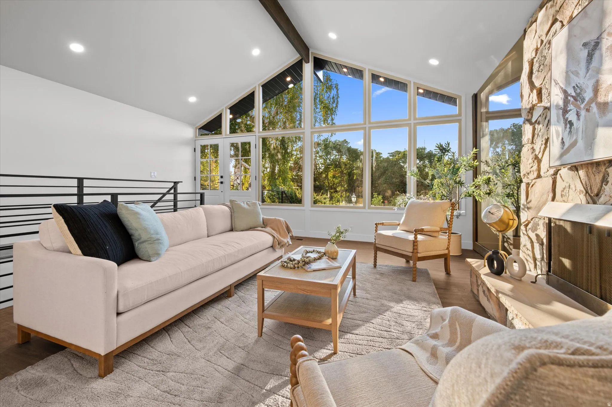 Spacious living area featuring a vaulted ceiling with exposed beams, recessed lighting, and expansive floor-to-ceiling windows