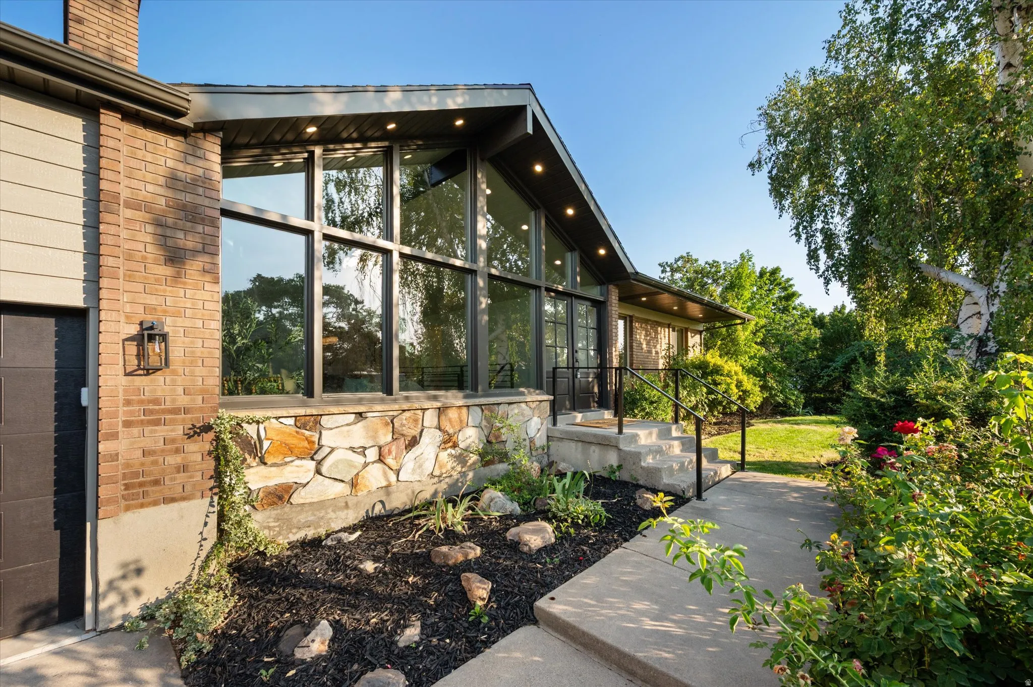 Contemporary exterior with a prominent brick chimney, large floor-to-ceiling windows, and a natural stone façade
