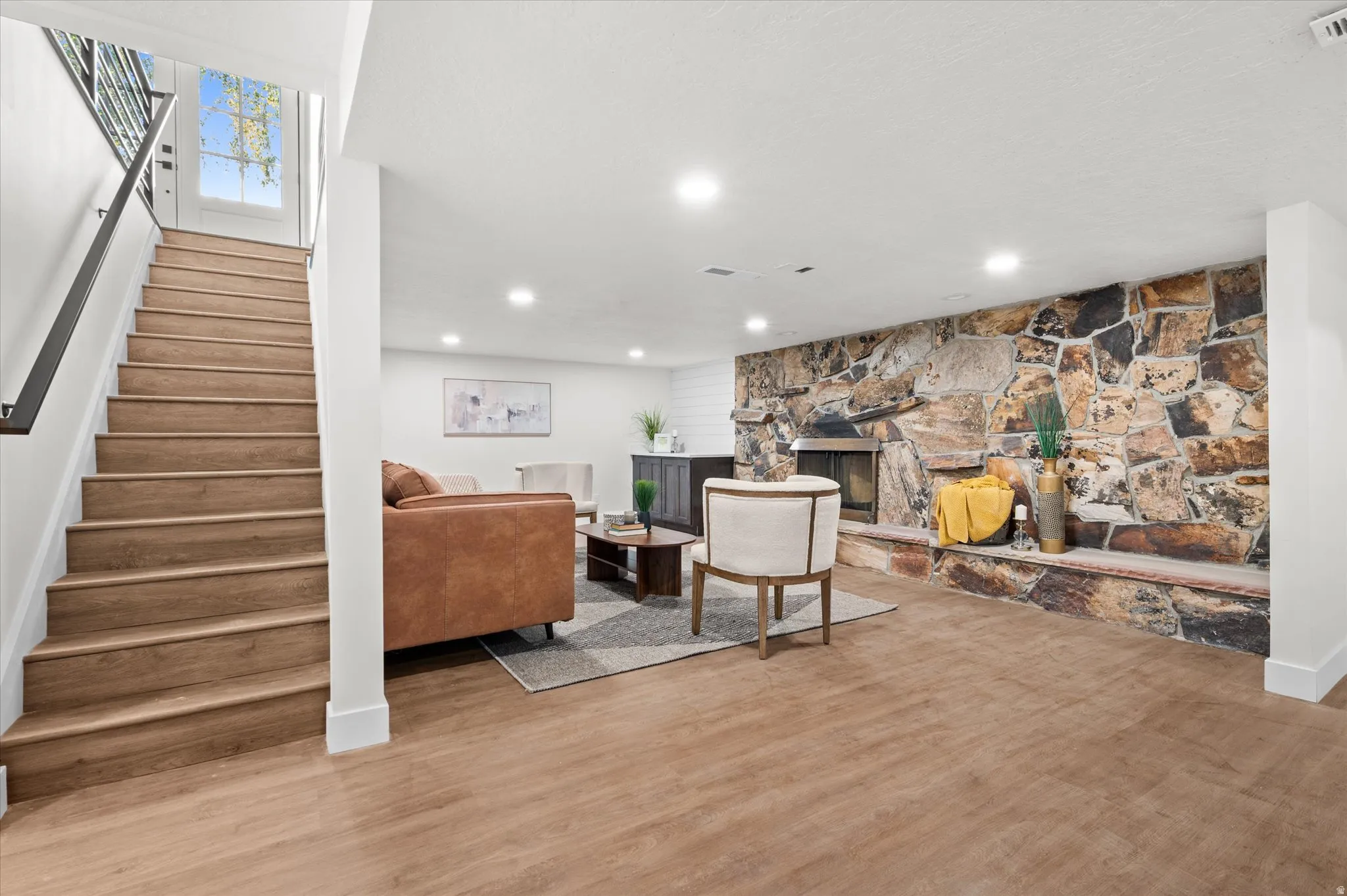 Finished basement featuring wood-finish flooring, recessed lighting, and a prominent stone accent wall with a built-in fireplace
