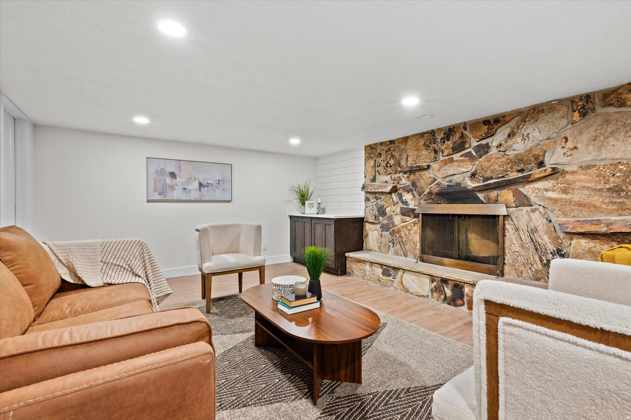 Stone fireplace with a hearth, wood-finish flooring, white walls, recessed lighting, and a built-in cabinetry