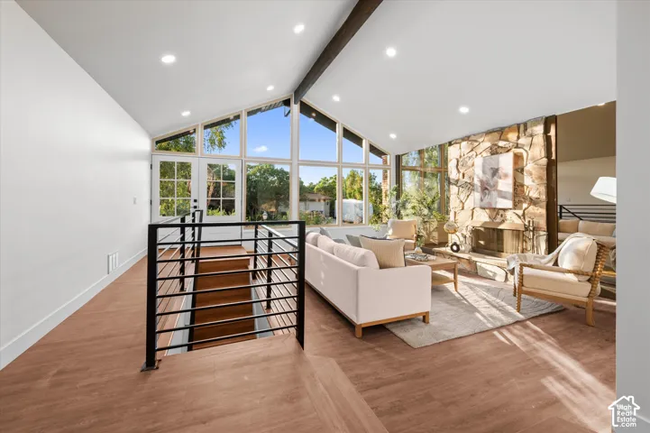 Vaulted ceilings with exposed wood beams, a stone-accented fireplace, and expansive windows characterize this living space