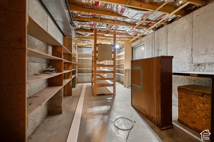 Unfinished basement space featuring concrete walls, exposed ceiling joists with insulation, and extensive built-in shelving